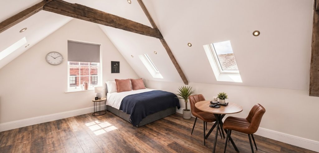 Interior view of luxury loft-style serviced apartments Worcester city centre featuring a modern kitchenette, exposed oak beams, and a plush sleeping area.